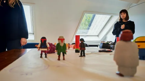 en avant plan différents objectifs sont posés sur une table (notamment des playmobiles et des ciseaux, de la colle, un minion) qui représente une situation clinique travaillée en formation, en arrière plan, les participantes de la formation qui observent la réalisation